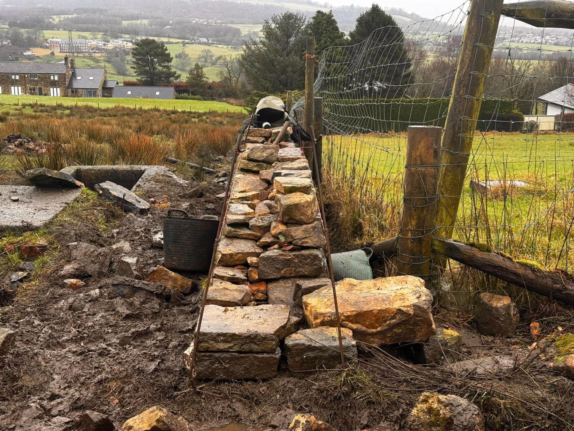 Dry stone field wall being built, with a batter gauge set over the wall to keep the correct slope
